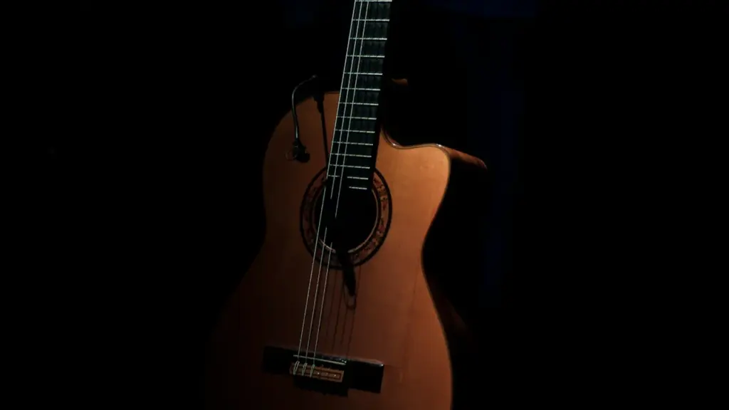 Guitarra acústica de madera en penumbra, evocando una velada íntima de flamenco y trovo.