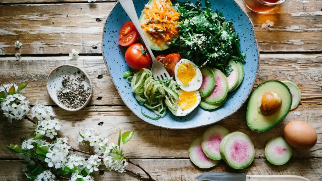 Plato colorido con verduras frescas, huevo poché y aguacate sobre mesa de madera.