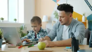 Padre ayudando a su hijo con el estudio mediante un ordenador en casa.