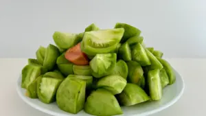 Un plato blanco con tomates verdes troceados listos para ser preparados en la cocina.