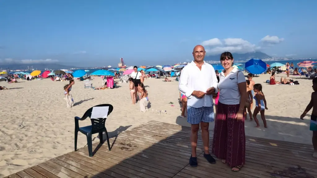 Hombre y mujer posan en una pasarela de madera sobre una playa con sombrillas.