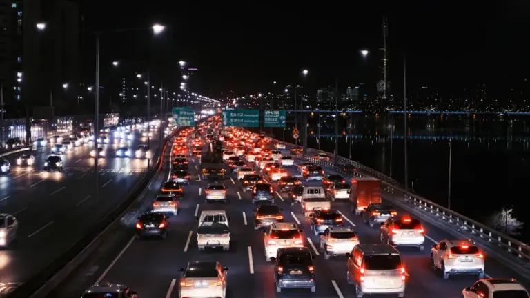 Coches circulando de noche por una autopista iluminada con intenso tráfico denso.