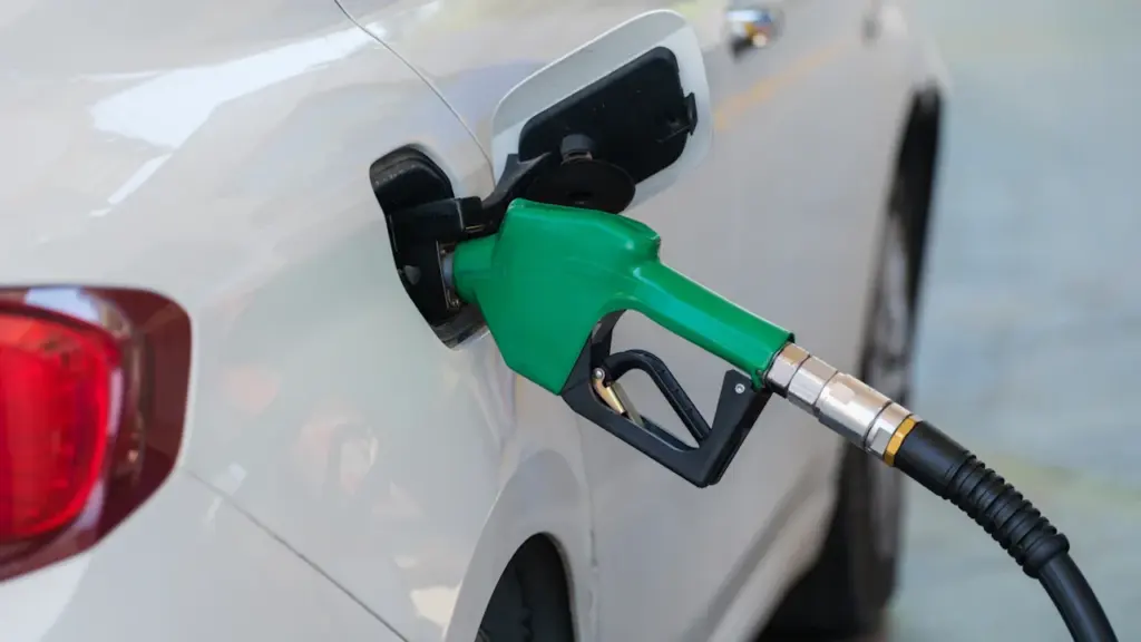 Primer plano de una manguera de gasolina repostando un coche blanco en la estación.