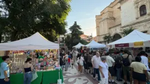 Varias carpas blancas instaladas en una plaza adoquinada con gente comprando mercancía diversa al aire libre.