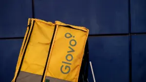 Mochila de reparto amarilla de Glovo contra una pared azul oscuro metálica.