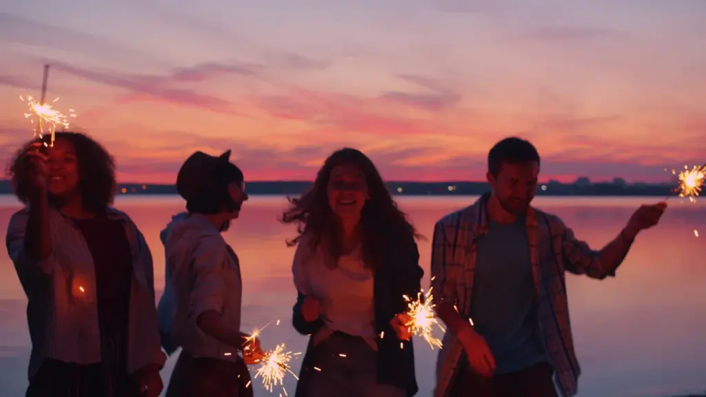 Grupo de amigos celebrando con bengalas durante un atardecer frente a un lago.