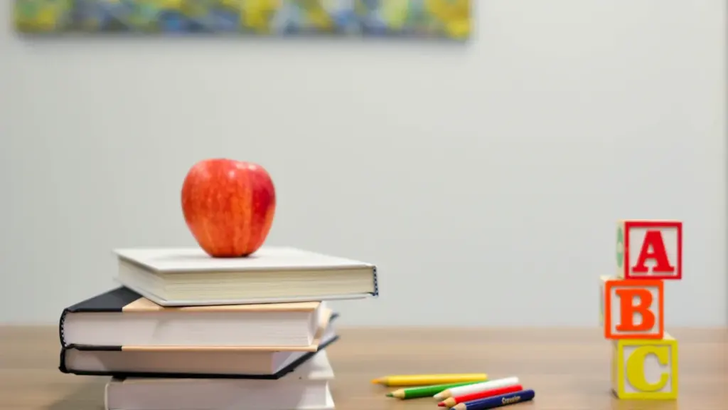 Pila de libros escolares con una manzana roja sobre una mesa de madera