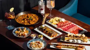 Mesa variada con platos de tapas, embutidos y bebida en restaurante español.